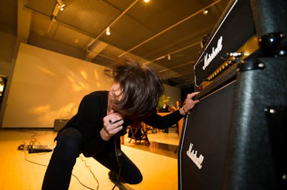 A person headbanging is singing into a microphone squatting down, holding onto the speaker